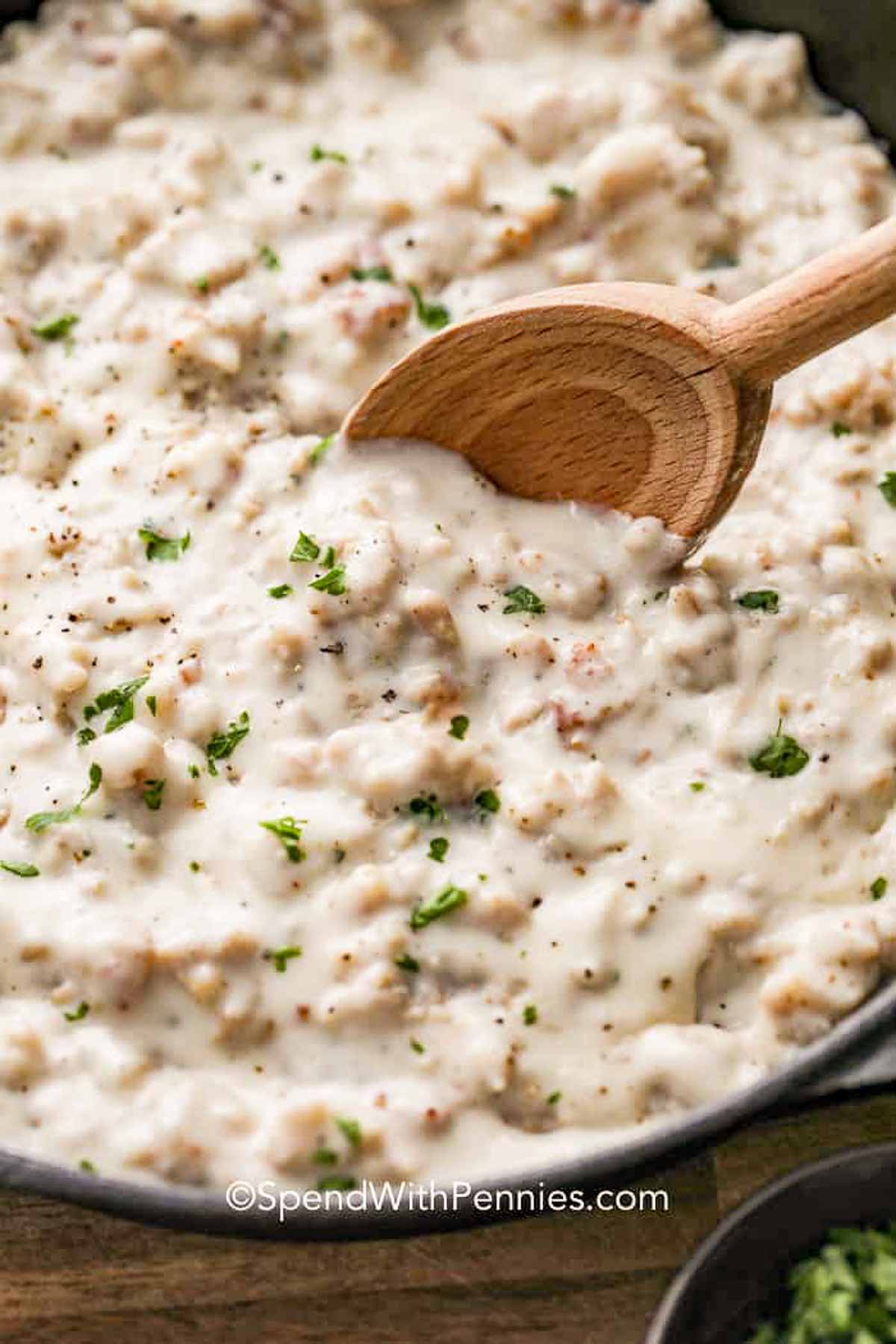 a skillet of sausage gravy with a wooden spoon