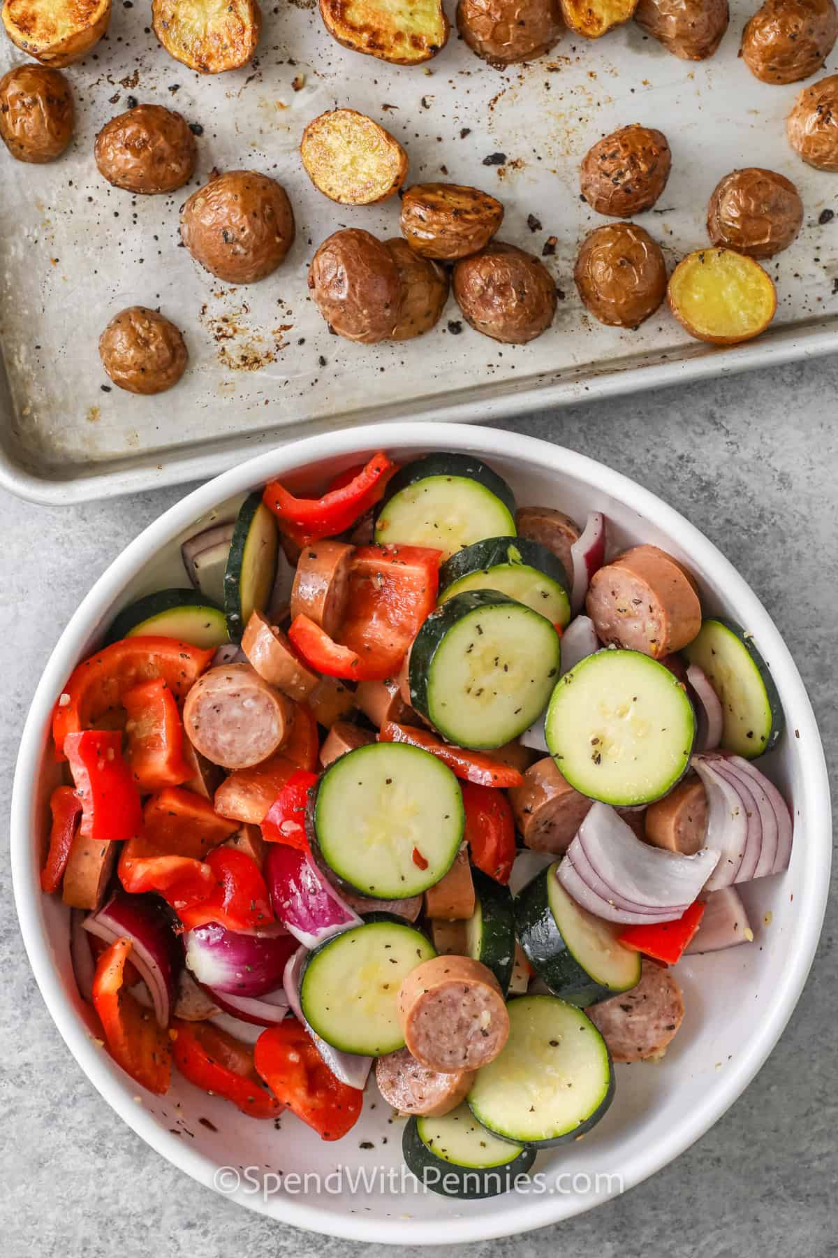 plate of vegetables and sheet pan of potatoes to make Roasted Sausage and Potatoes