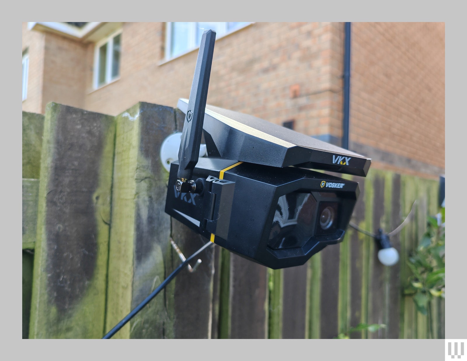 Black angular outdoor security camera with antenna attached to wooden fence