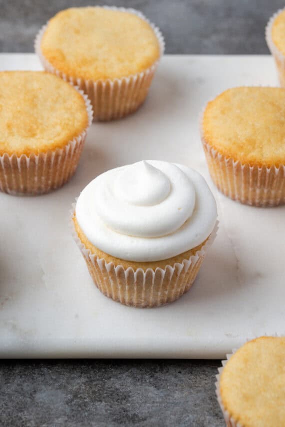 An almond cupcake topped with a swirl of coconut frosting, surrounded by unfrosted cupcakes.