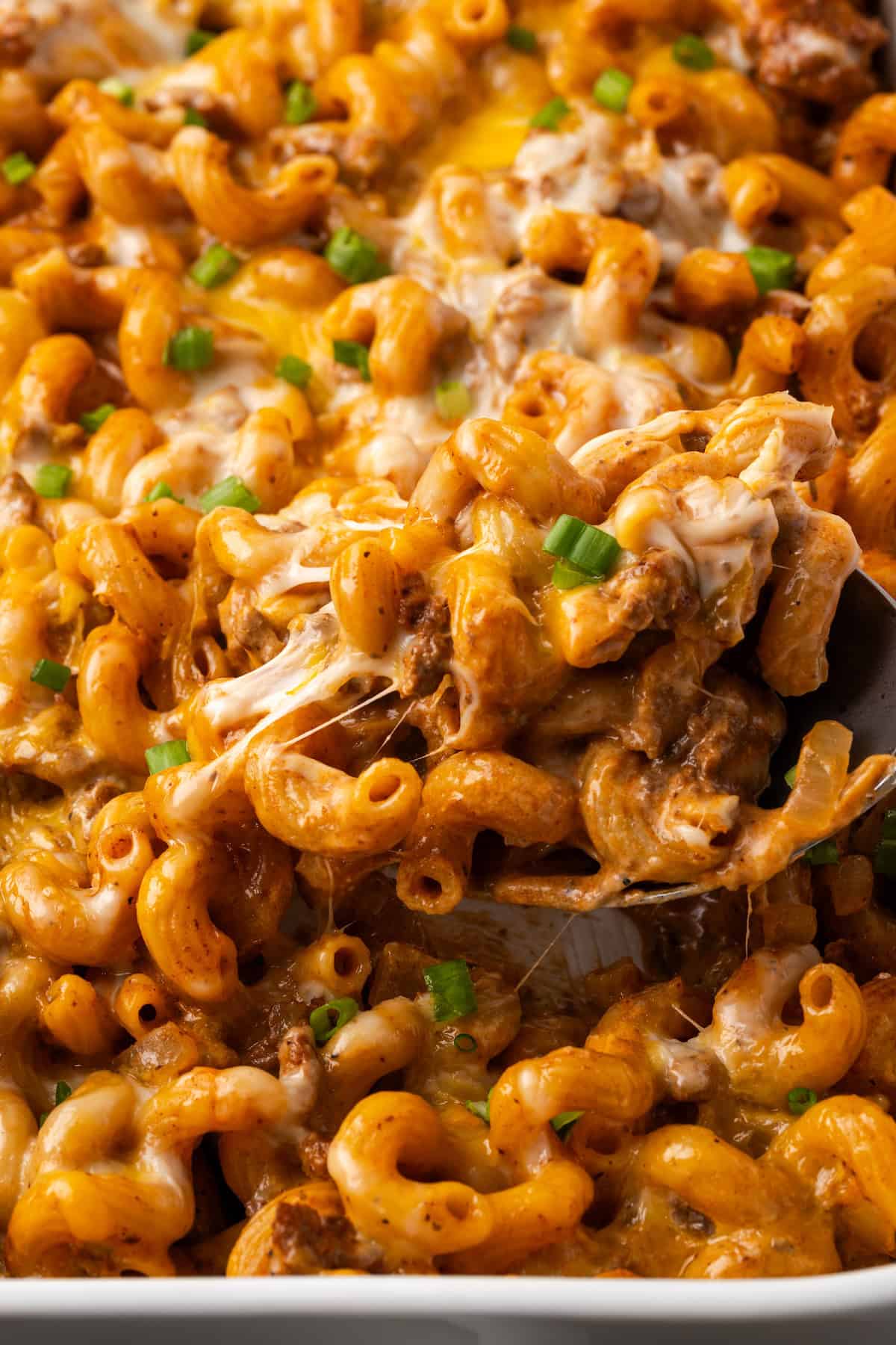 Close up of a spoon scooping cheeseburger casserole from a ceramic baking dish.