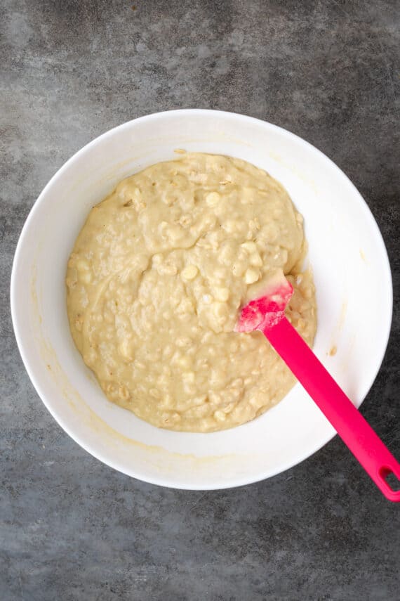 Cinnamon muffin batter in a large white bowl with a red spoon.