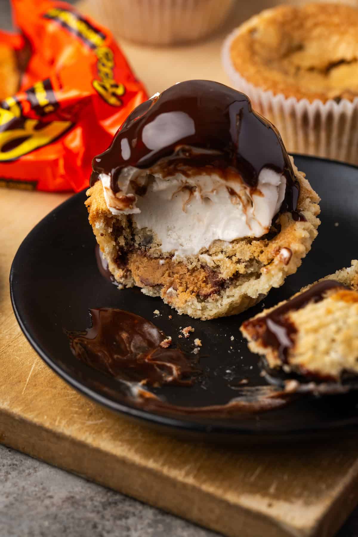 A cookie cup topped with a scoop of ice cream and chocolate fudge sauce cut in half on a black ceramic plate.