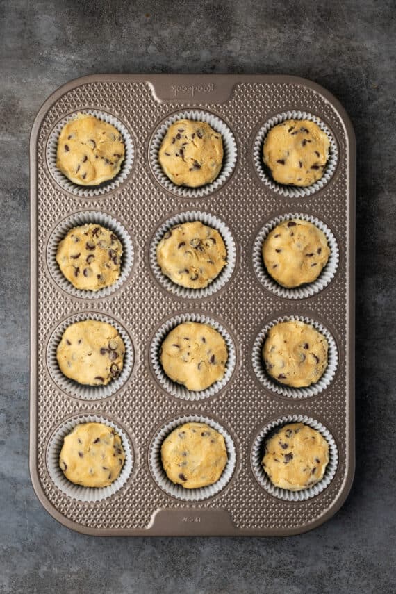 Overhead view of unbaked cookie cups inside a 12-well muffin tin.