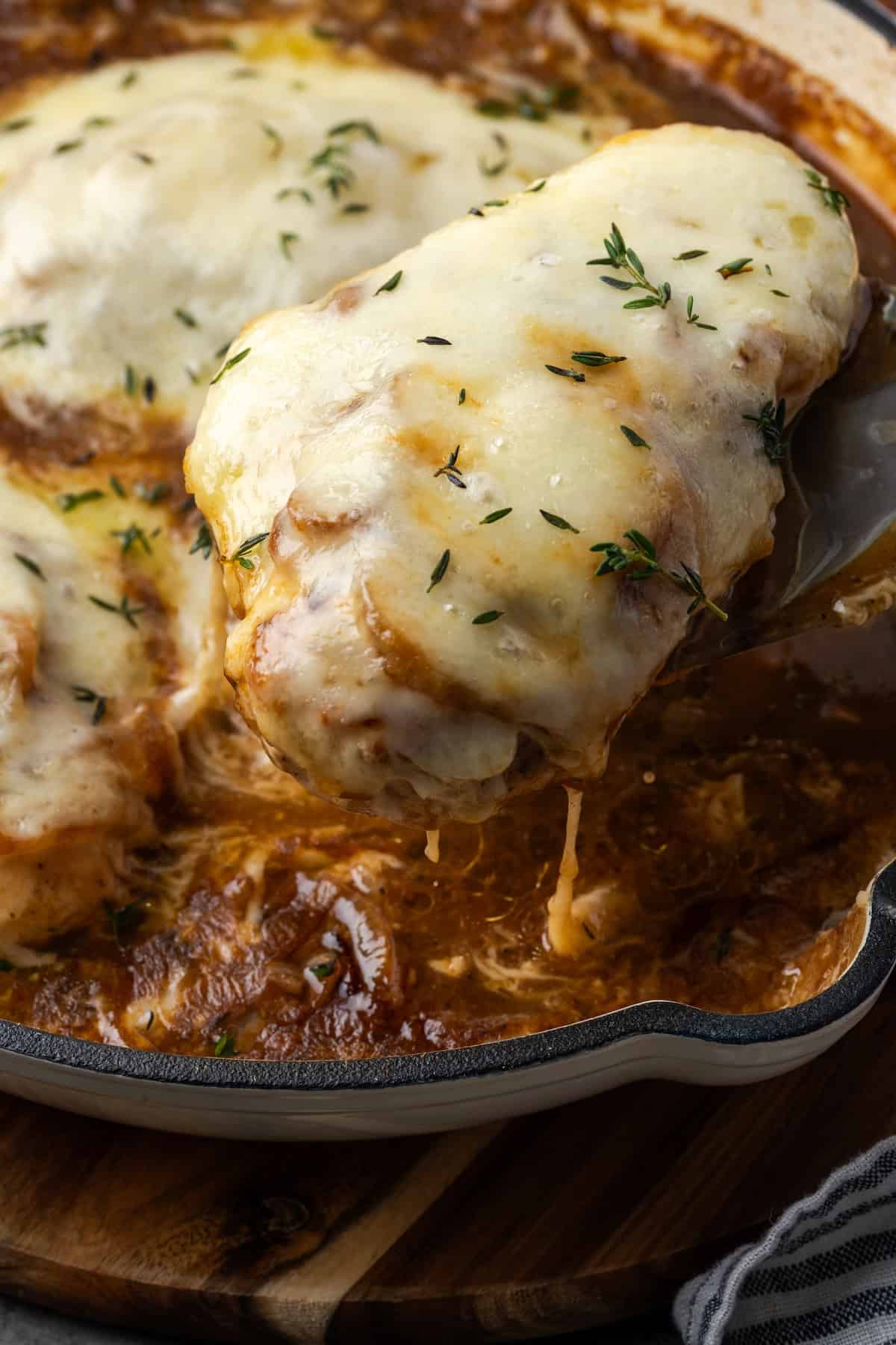 Close up of a French onion chicken breast covered with cheese being lifted from a skillet.