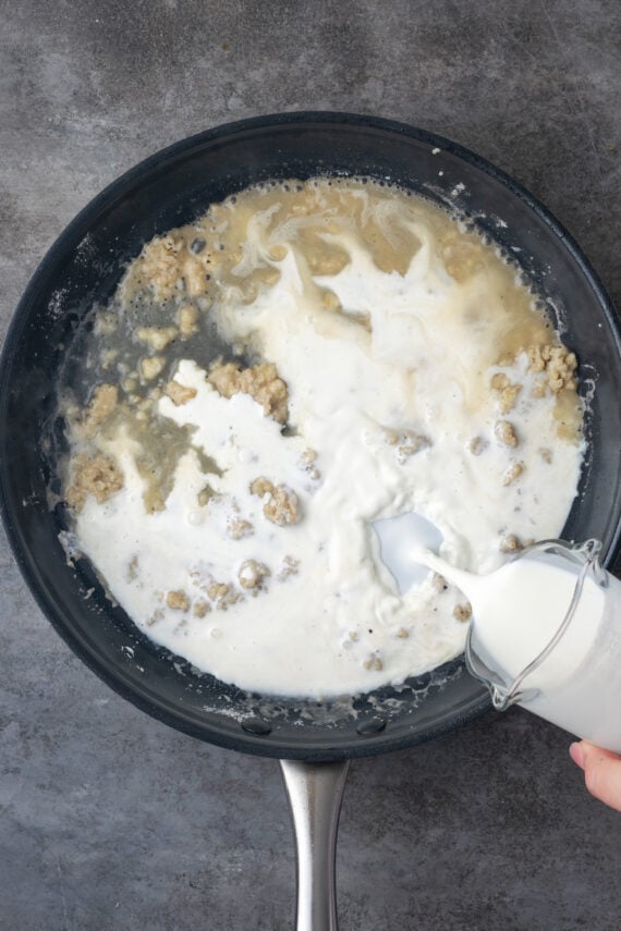 Milk being poured into a roux of butter and flour inside a skillet.