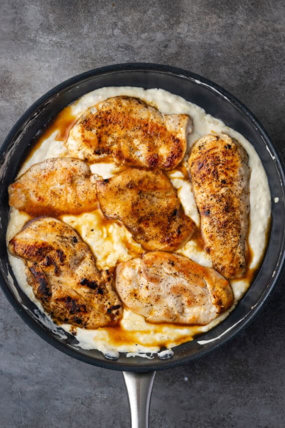 Cooked chicken breasts nestled back into a skillet with the garlic parmesan sauce.