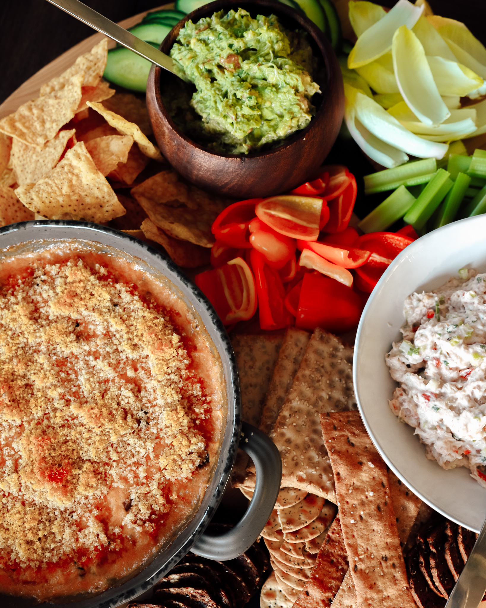 A charcuterie board of three dips, including guacamole and crab dip