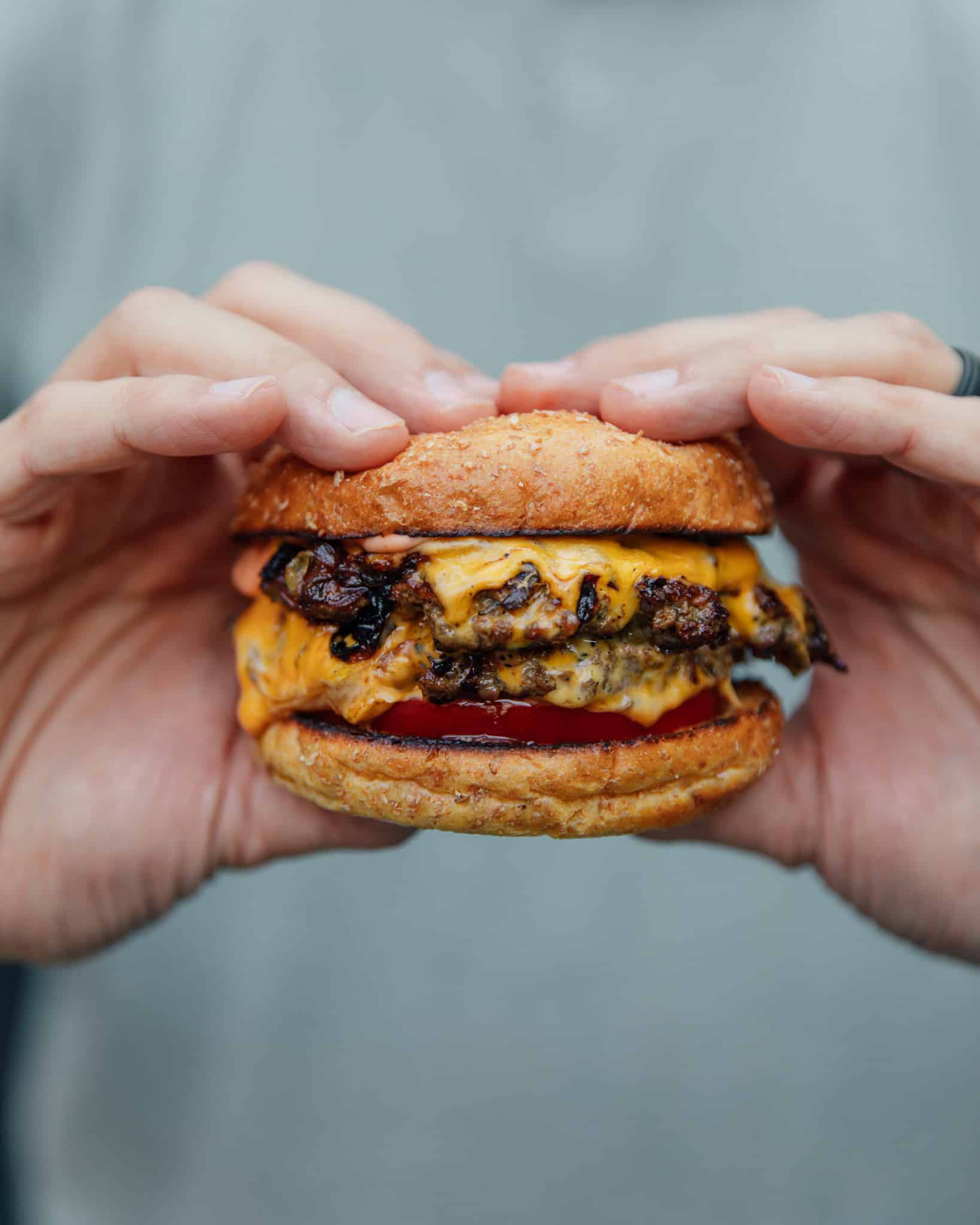 Two hands holding up a delicious, juicy Smashburger on a bun with a tomato slice