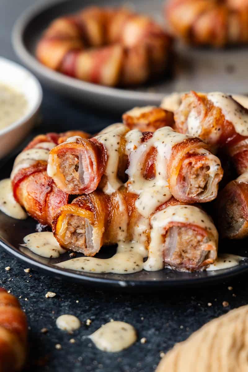 A plate of halved stacked bacon wrapped sausage filled onion rings, topped with a white sauce.