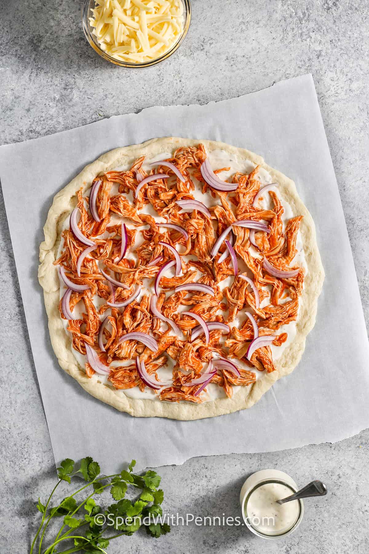 shredded chicken in sauce with red onions on dough to make Buffalo chicken pizza.