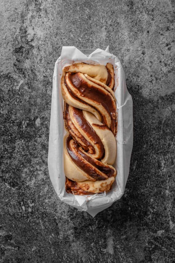 Overhead view of an unbaked chocolate babka inside a lined loaf pan.