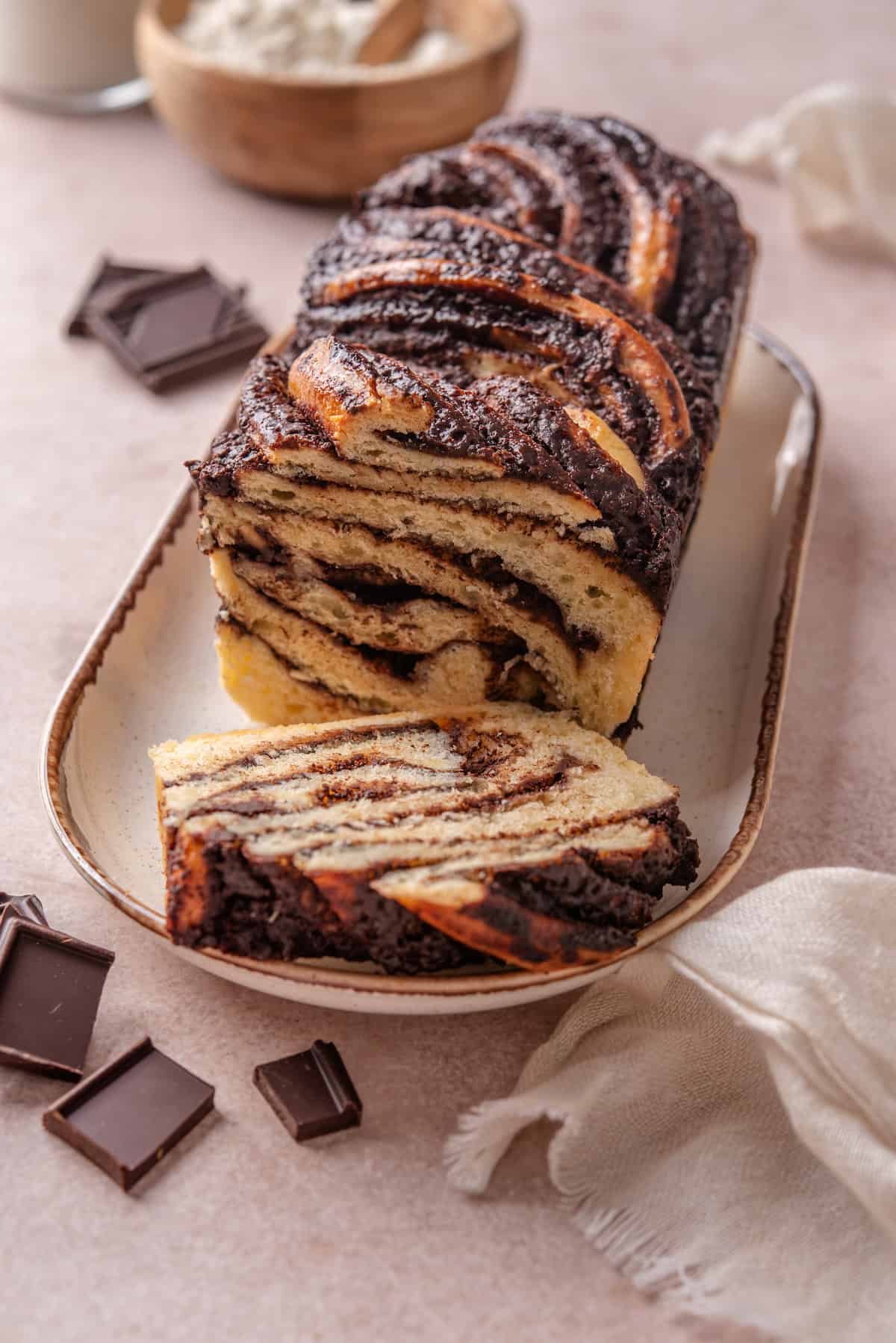 A chocolate babka on a long plate with a slice cut from the end.