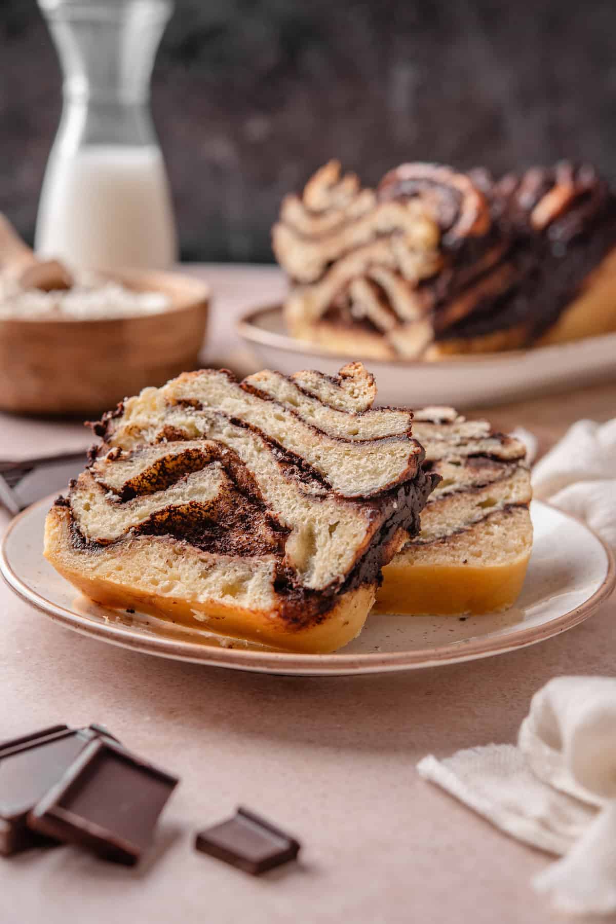 Two slices of chocolate babka on a plate with the rest of the babka in the background.