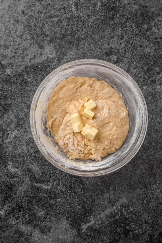 Cubed butter added to the dough ingredients in a glass bowl.