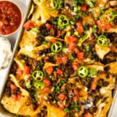 baked homemade nachos on a pan topped with jalapenos and sour cream