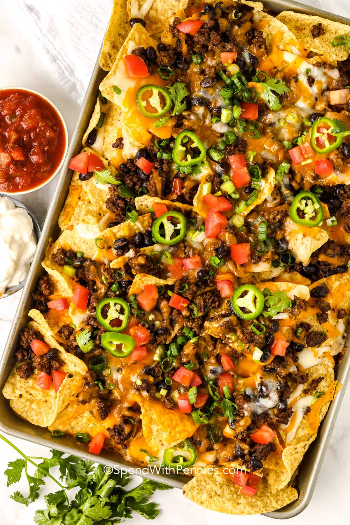 baked homemade nachos on a pan topped with jalapenos and sour cream