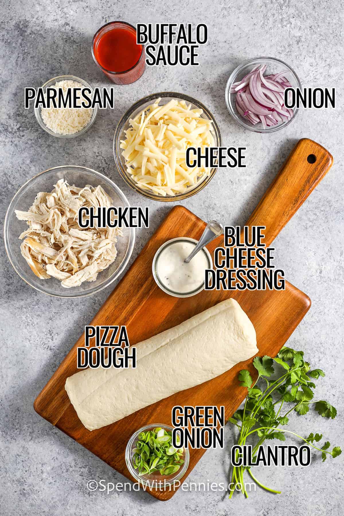 Ingredients to make Buffalo chicken pizza, with labels, including Buffalo sauce, onion, cheese, parmesan, chicken, blue cheese dressing, pizza dough, green onion, cilantro