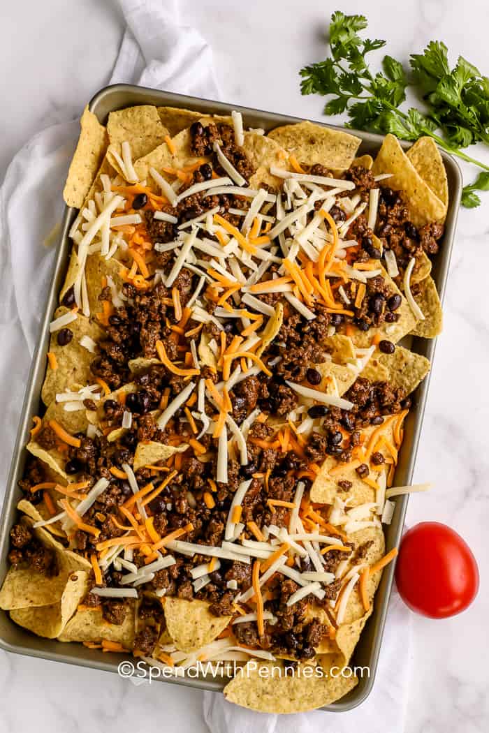 nacho chips, cheese, meat and beans on a baking sheet for nachos