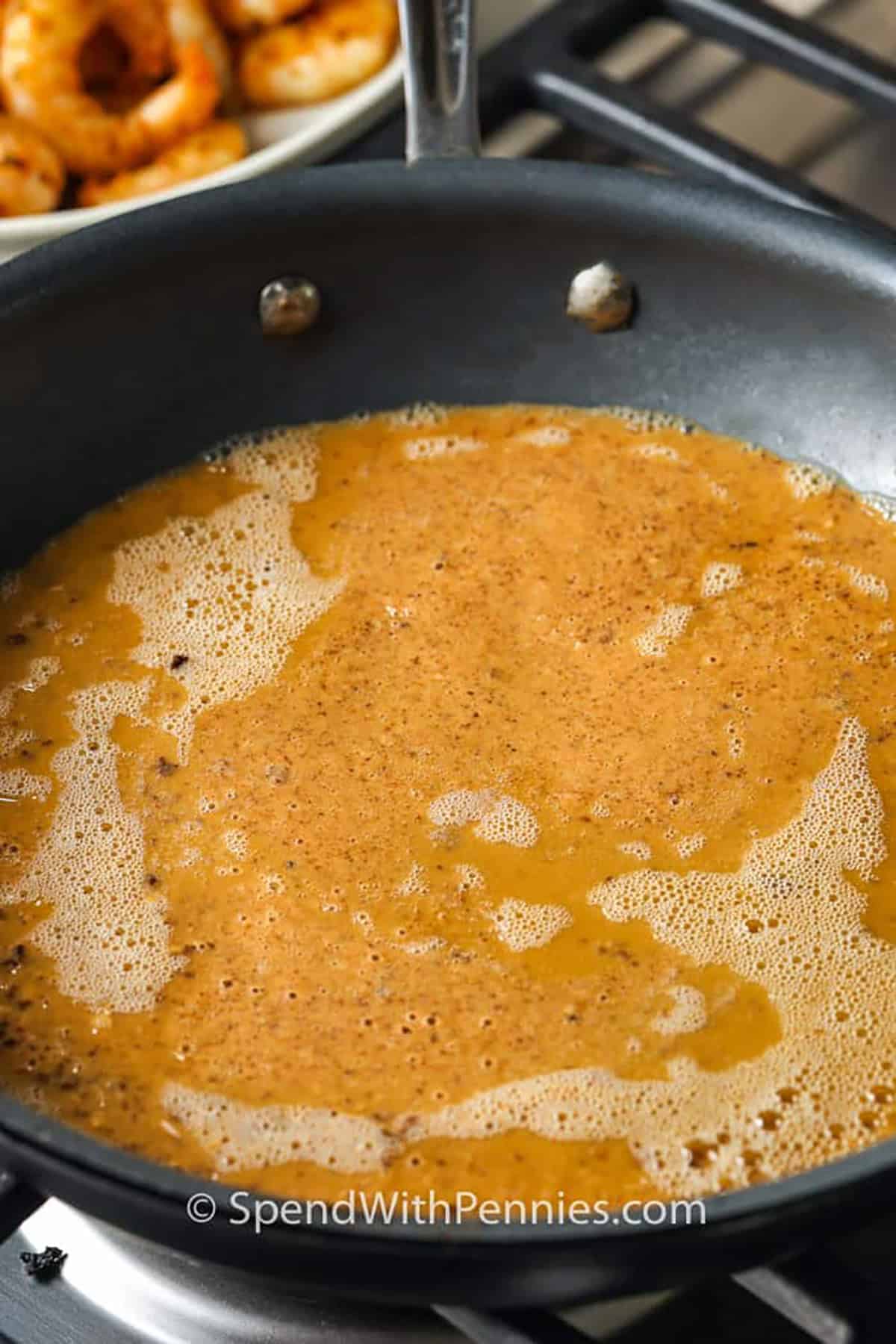 Adding broth to the finished roux in a pan to make shrimp etouffee.