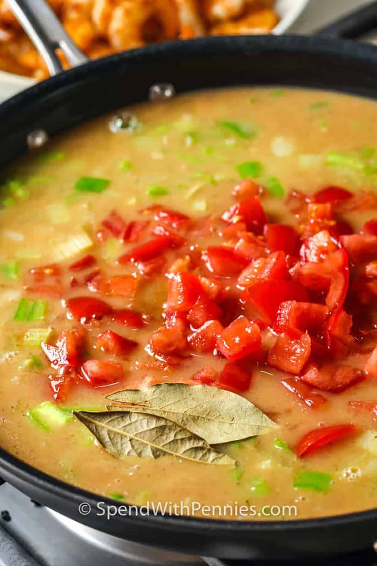 Adding tomatoes to the sauce in a pan, to make shrimp etouffee.