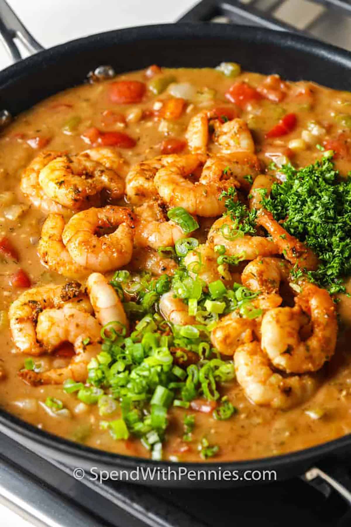 Adding green onion and parsley garnishes to a pan of shrimp etouffee.