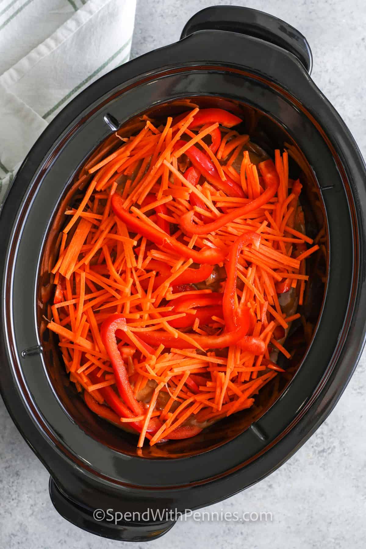 adding julienned carrots and red bell peppers to a slow cooker to make peanut noodles