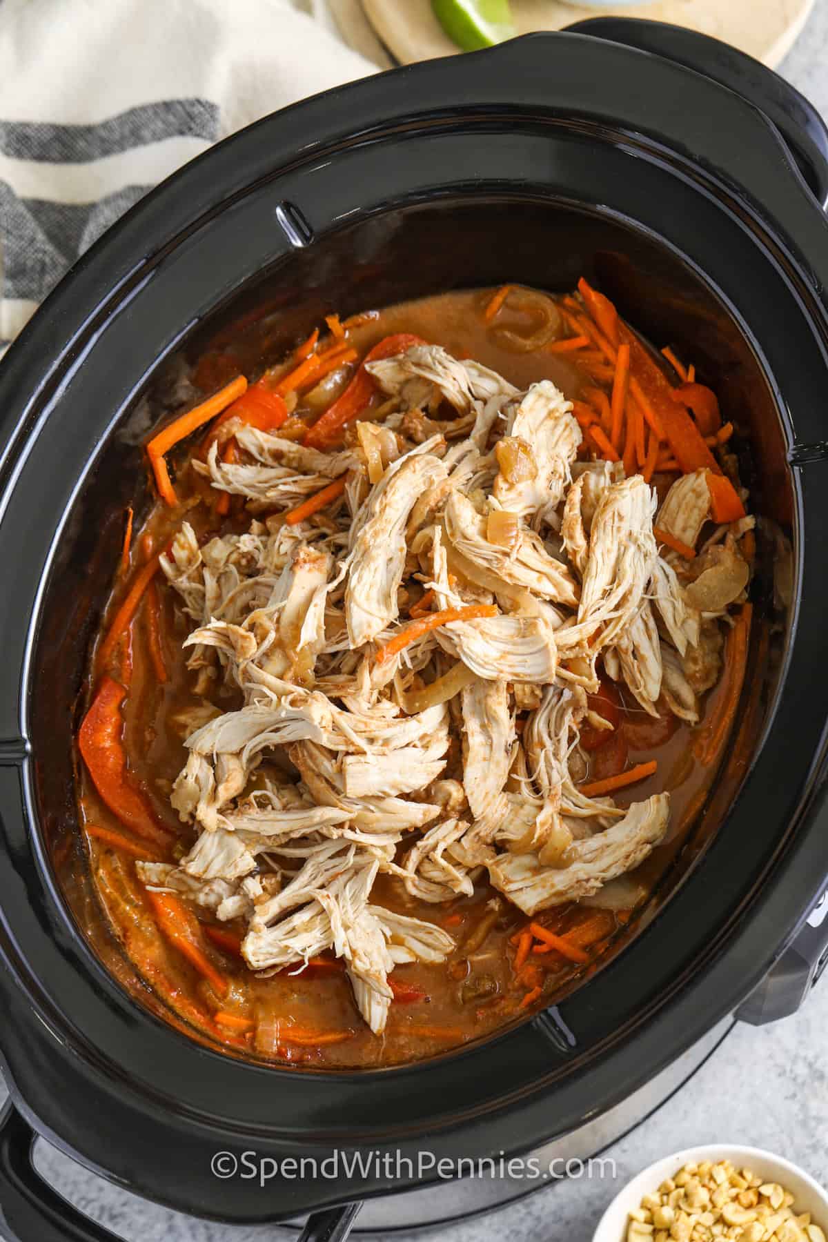 Adding shredded chicken to a slow cooker to make peanut noodles.