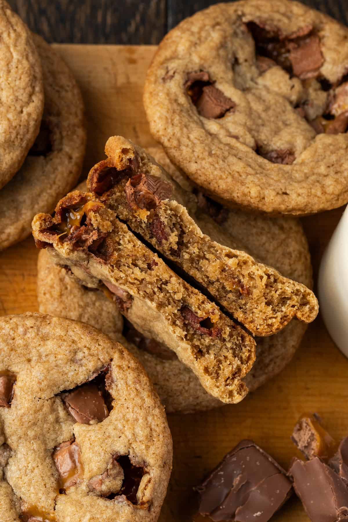 Overhead view of Milky Way cookies stacked on a wooden cutting board, with one cookie broken in half.