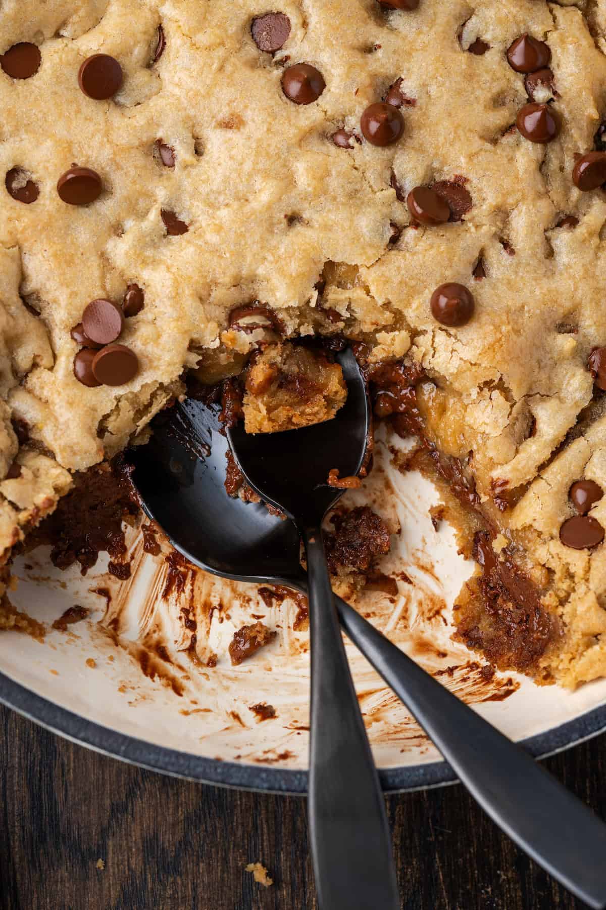 Overhead view of a skillet chocolate chip cookie with a serving missing and a spoon resting in the open space.